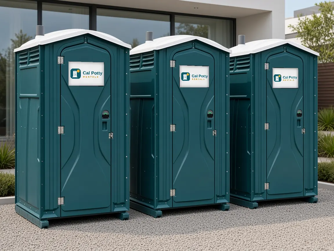 Three teal portable toilets in a row on gravel in front of a modern glass-walled building